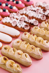 different types of eclairs decorated with cream and pistachio isolated on pink background