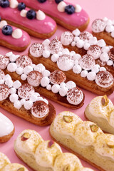 different types of eclairs decorated with cream isolated on pink background