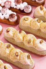 eclairs decorated with cream and pistachio isolated on pink background