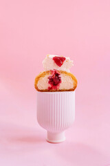 Gourmet French Shu cake with white cream and jam cut in half on a white stand isolated on pink background