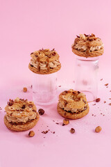 Paris Brest French dessert filled with nut and almond creme mousseline sprinkled with hazelnuts on the glasses and on the surface of pink color