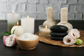 Massage bags, spa stones, sea salt, burning candles and flowers on wooden table