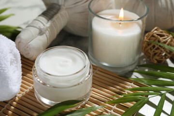 Spa composition with different cosmetic products, herbal bags, burning candle and leaves on table, closeup