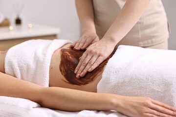 Woman undergoing chocolate body wrap treatment in spa salon, closeup