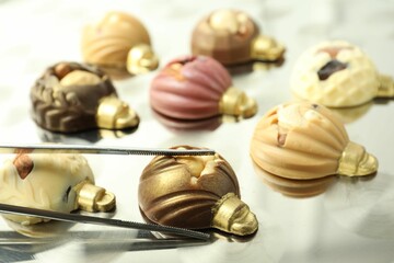 Tweezers with different sweets in shape of baubles on light table, closeup