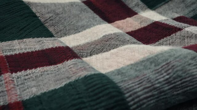 Discover the inviting texture of plaid wool fabric featuring a blend of soft gray, rich green, and deep red hues. Observe the detailed pattern and gentle focus shifts that highlight craftsmanship.
