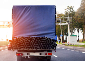 A tilt van transports an oversized cargo of metal pipes along the road against the backdrop of a...