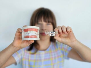 Dental health demonstration showcasing model teeth and clear aligner held by a young woman indoors
