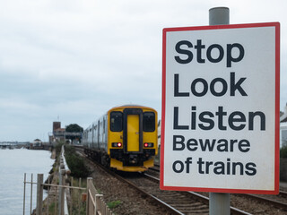 Obraz premium Warning sign for pedestrians next to riverside railway lines in a Devon village UK