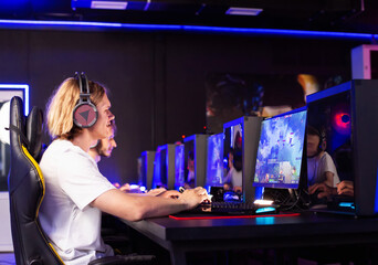 Five Caucasian gamers of different ages are playing strategy game in computer club. Multiplayer online game in modern cyber space cafe with desktop computers. Cyber team plays shooter, tournament