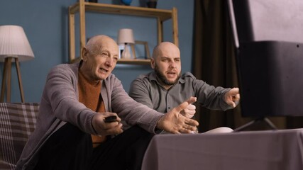Two fans father and son sitting on a couch watch soccer game on TV, celebrate victory favorite team winning championship.