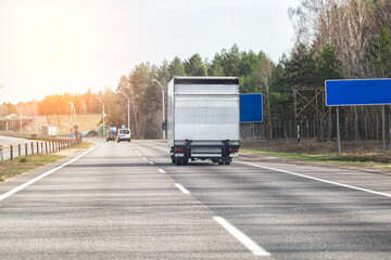 Naklejka premium A modern van with a tail lift is driving along an asphalt road against the backdrop of a sunset. Concept of road transport of trucks with hydraulic lift. Copy space for text