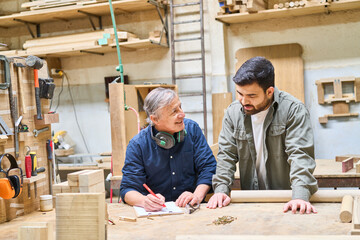 Young apprentice learning woodworking skills from experienced craftsman