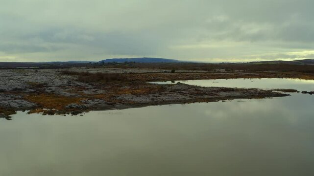 Aerial shot ascending large Turlough, reflecting sky, revealing rocky terrain. Burren national park