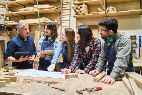 Young apprentices and mentor discussing woodworking project in lumberyard