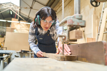 Young woman operating machinery in a bustling lumberyard workshop