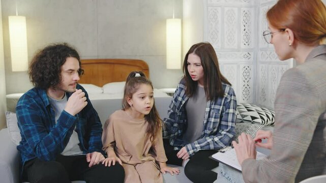 In a cozy, bright apartment, a girl talks to a young female psychologist, sharing details about her parents, who argue slightly in the background. The psychologist listens attentively, creating a
