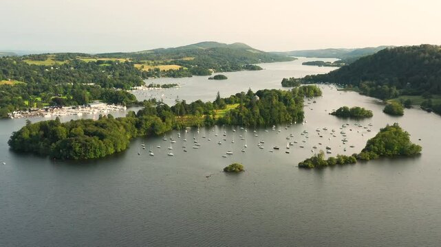 Windermere in Lake District National Park, Cumbria, England. Aerial video fly in to south over Belle Isle near Bowness. Yacht moorings. Summer evening
