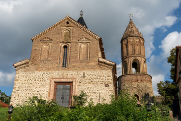 Fototapeta premium A large stone building with a steeple and a small door. The building is surrounded by bushes and trees