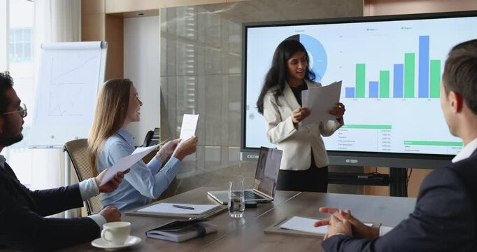 Indian businesswoman distributing printed reports or data sheets among seminar, negotiations participants, or colleagues during presentation for detailed reviewing information, learn specific points