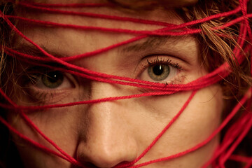 Close up of part of female face with light wrinkles and big green eyes, her head covered with red...