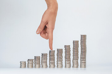 Female finger shows coin in middle column. Columns of silver coins in growth. Investing and business development.