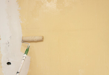 Painting a wall with a roller in light yellow, showing the process of interior design, home improvement, or wall renovation.