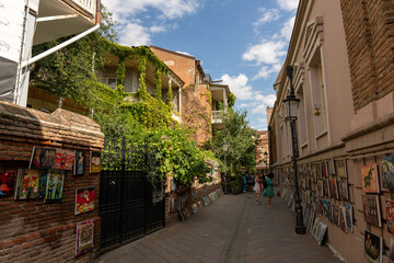 Fototapeta premium A narrow street with a lot of pictures on the wall. A woman is walking down the street
