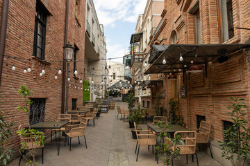 A brick street with tables and chairs outside of a restaurant. The tables are empty and the chairs are lined up