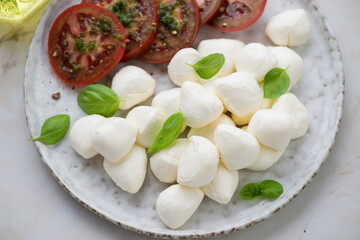 Grey plate with mini mozzarella cheese, green basil and dark-red tomatoes, horizontal shot, middle close-up, selective focus