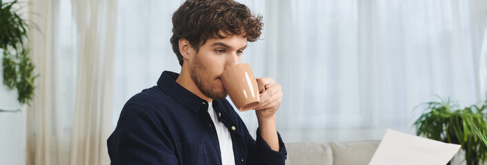 Curly-haired young man sips from a mug as he engages in work at home, banner
