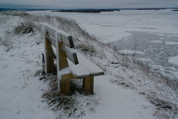 bench in the snow on a high bank near a frozen river