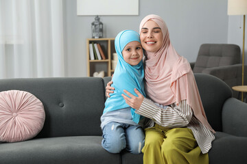 Obraz premium Muslim mother and her daughter sitting on sofa at home, space for text