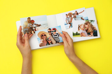 Woman with open photo album and different photos on yellow background, top view