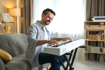 Smiling man playing synthesizer at home. Electronic musical instrument