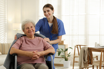 Fototapeta premium Caregiver covering senior woman with blanket indoors. Home health care service