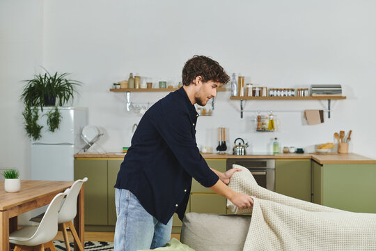 A young man tidies up his cozy living room while dressed in a stylish shirt. - Powered by Adobe