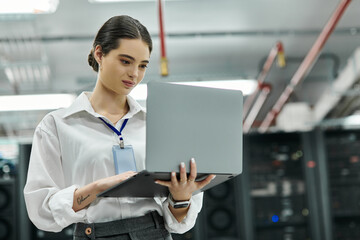 IT specialist reviews data on her laptop in a high-tech server room environment.