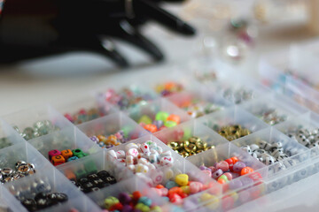 Hand figurine, colorful friendship bracelets, necklaces, various beads and DIY supplies on the table. Making jewelry at home. Selective focus.
