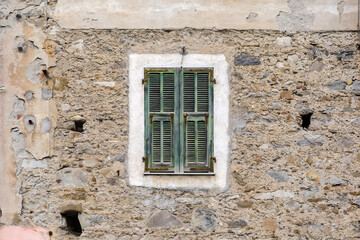 Ancient stone wall with window covered with wooden exterior shutters