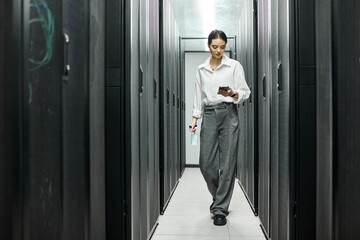 Fototapeta premium A woman in a white shirt navigates through a server room, engaging with technology.