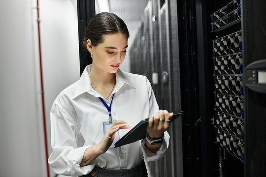 A dedicated woman in a white shirt works on a tablet in a bustling server room.