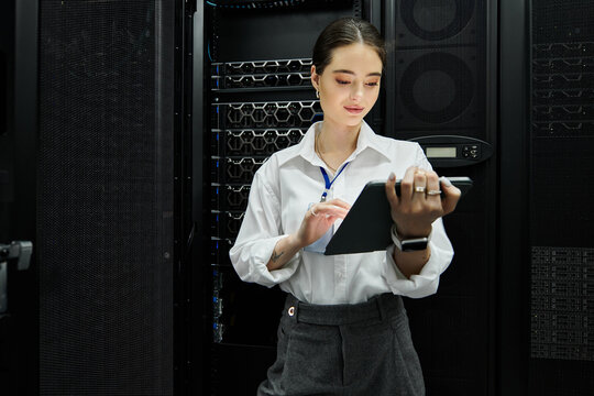 A woman in a white shirt diligently works in a sleek server room, engaging with technology.