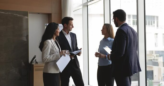 Four young multiethnic teammates lead conversation, reviewing client feedback, requirements, or concerns after negotiations or formal meeting, met in conference room. Collaboration, teamwork, briefing