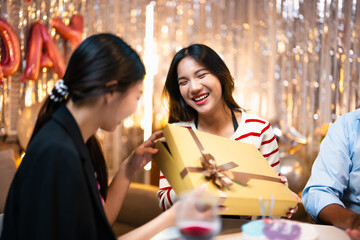 Asian friends throwing surprise birthday party for asian woman, giving her thoughtful gift in living room. Cheerful group of people celebrating birthday anniversary, gifting  present
