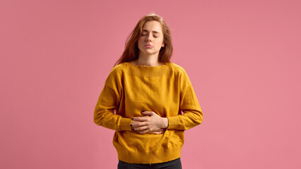 Young red-haired woman i a yellow sweater holding her stomach in pain, suffering from gastritis,...