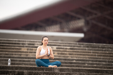 Obraz premium A woman is sitting on a set of stairs, meditating. Concept of calm and tranquility, as the woman focuses on her breathing and clears her mind. The setting of the stairs adds a sense of elevation