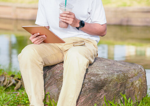 Asian businessman using digital tablet and phone, working outside in a park. Business, people, concept. Young man using internet, working online outside. Lifestyle business workplace 