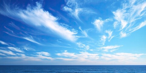 Obraz premium Vibrant blue summer sky with wispy white clouds stretching across the horizon above a serene ocean view under bright daylight
