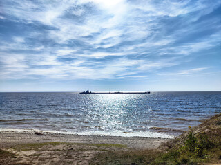Calm water reflects sunlight with a distant barge near the shoreline under a clear sky
